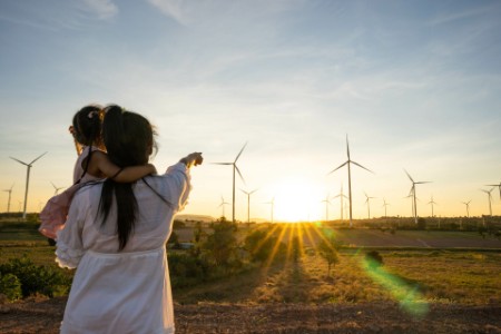 Kvinde med barn på armen peger på vindmøller i solnedgang