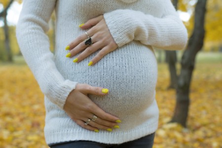 Kvinde i hvid striksweater holder med hænder på gravid mave