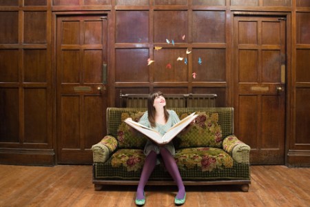 Ung kvinde sidder i sofa og læser i en stor bog