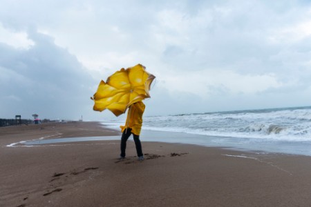 Mand med gul paraply på strand i stormvejr