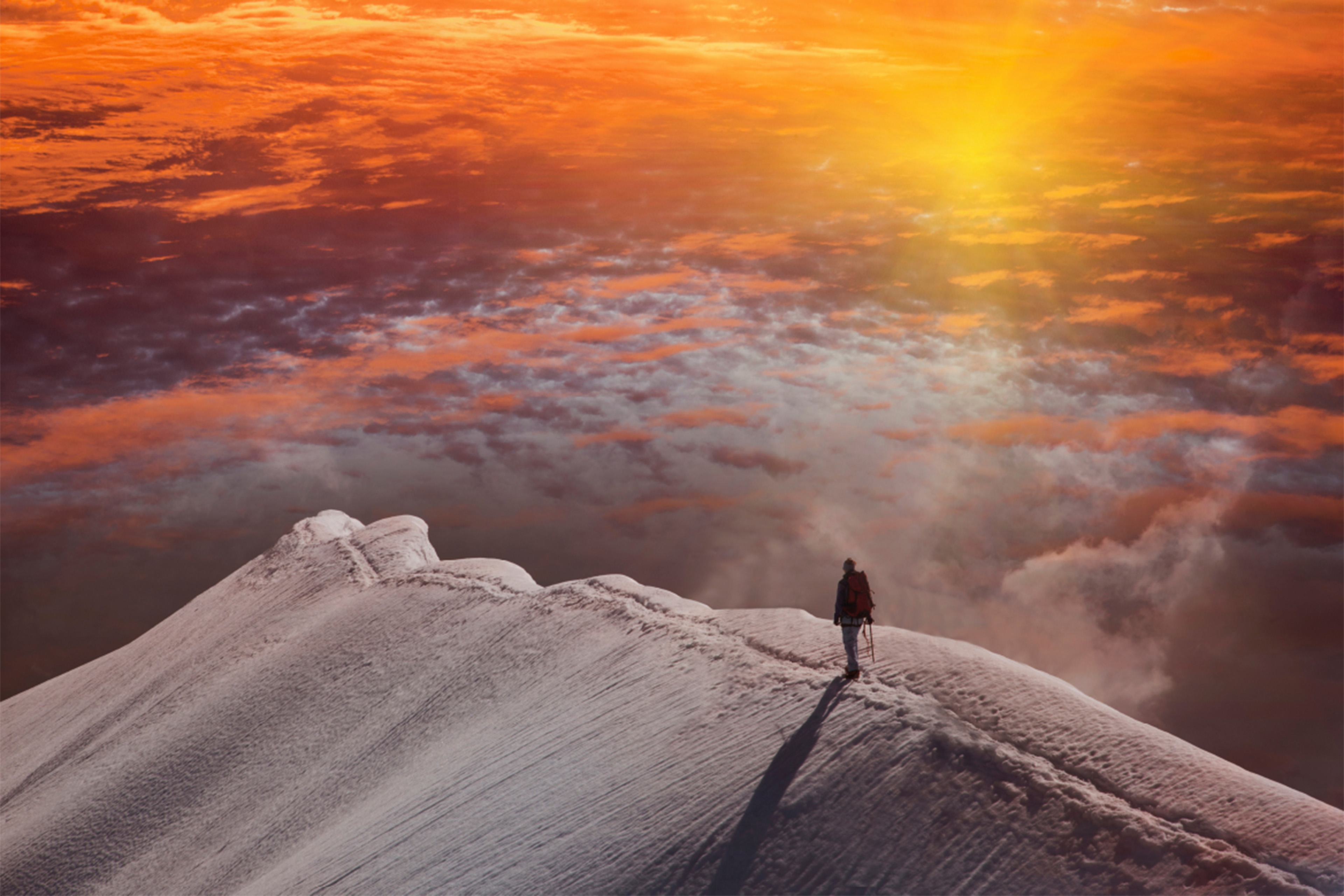 Mand vandrer på smal bjergryg i solnedgang