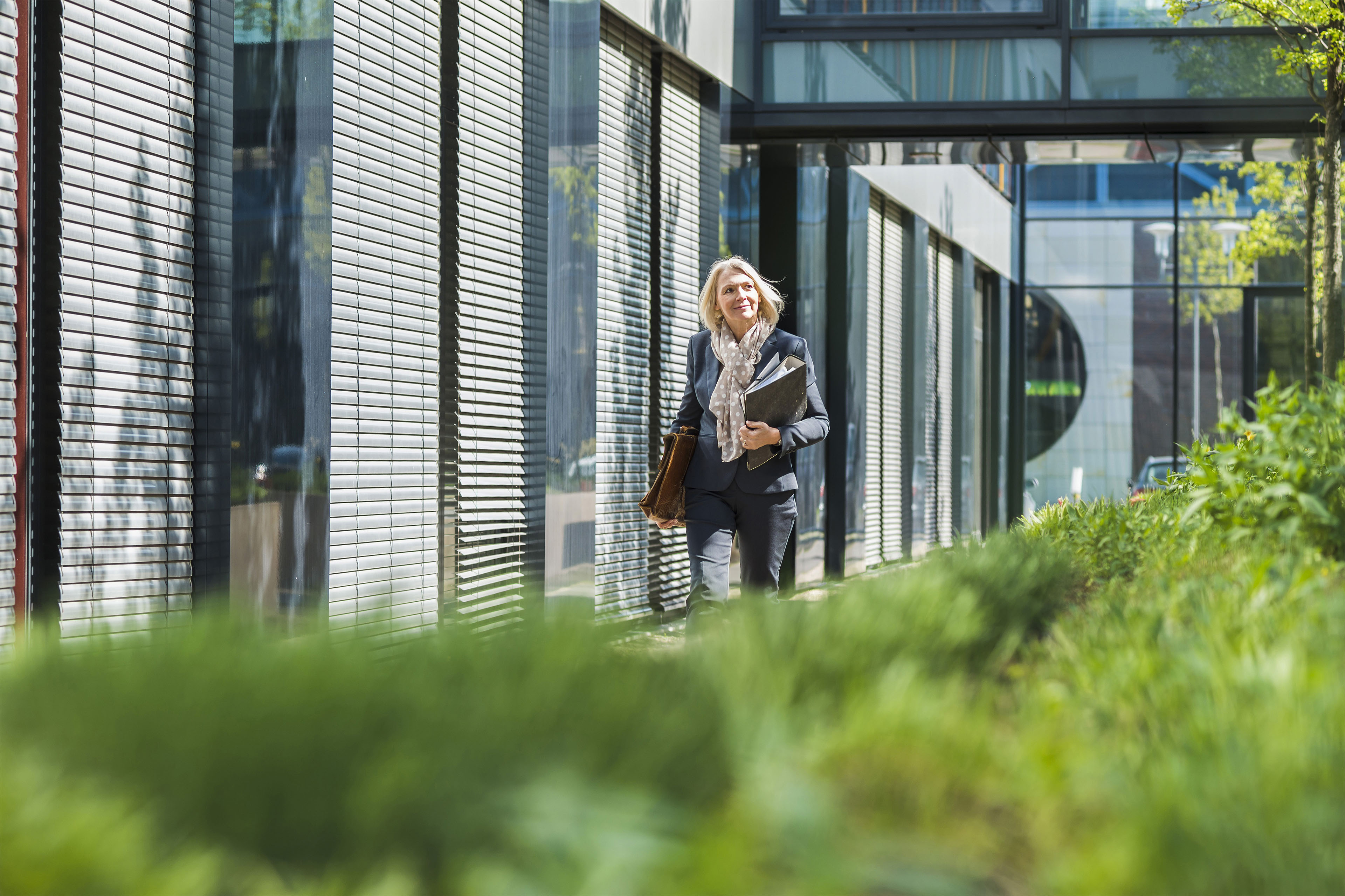 Forretningskvinde går langs moderne bygning i solskin