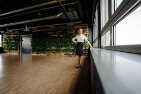Forretningskvinde står i kontor med plantevæg og ser ud ad vinduet.