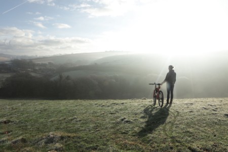 Kvinde med cykel kigger ud over landskabet en frostklar morgen