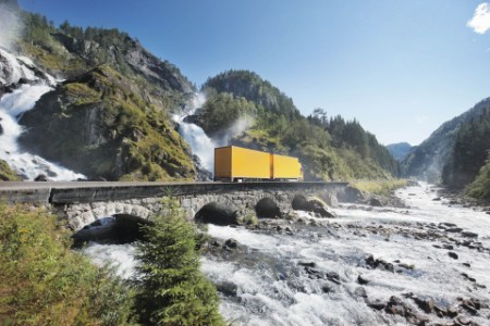 Gul lastbil kører over bro ved vandfald