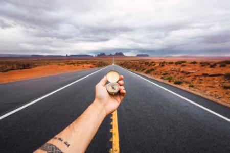 Eine Hand hält einen Kompass über die Straße zum Monument Valley