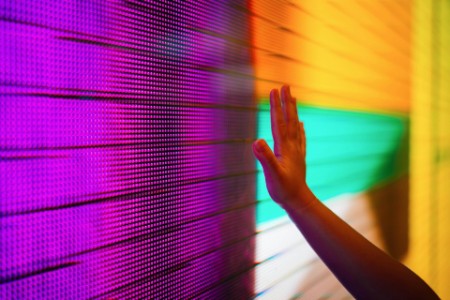 Nahaufnahme einer Kinderhand, die einen beleuchteten und mehrfarbigen LED-Bildschirm berührt, der eine Verbindung zum Zukunftskonzept herstellt