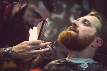 Barbier trimmt Bart eines bärtigen Mannes im Barbershop