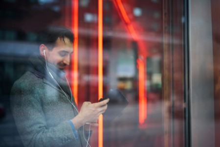 Eleganter Mann mit Smartphone, das sich im Fenster spiegelt