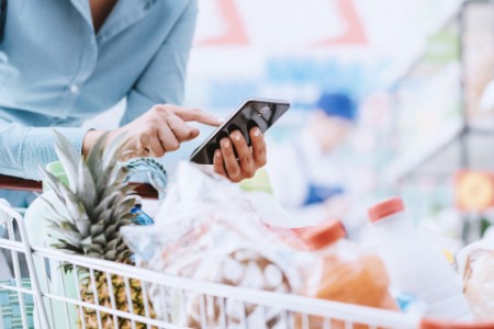 Frau, die mit ihrem Smartphone in einem Supermarkt Lebensmittel einkauft. 