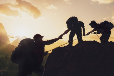 Junge asiatische drei Wanderer klettern auf den Gipfel des Berges in der Nähe von Berg. Menschen helfen sich gegenseitig beim Aufstieg auf einen Berg bei Sonnenaufgang. Eine helfende Hand geben. Klettern. Helfen und Teamarbeit Konzept