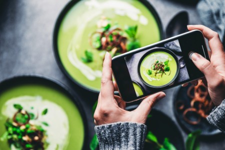 Frau fotografiert frische grüne Suppe -  Close-up of a woman taking a photo of green cream soup with her mobile phone.
