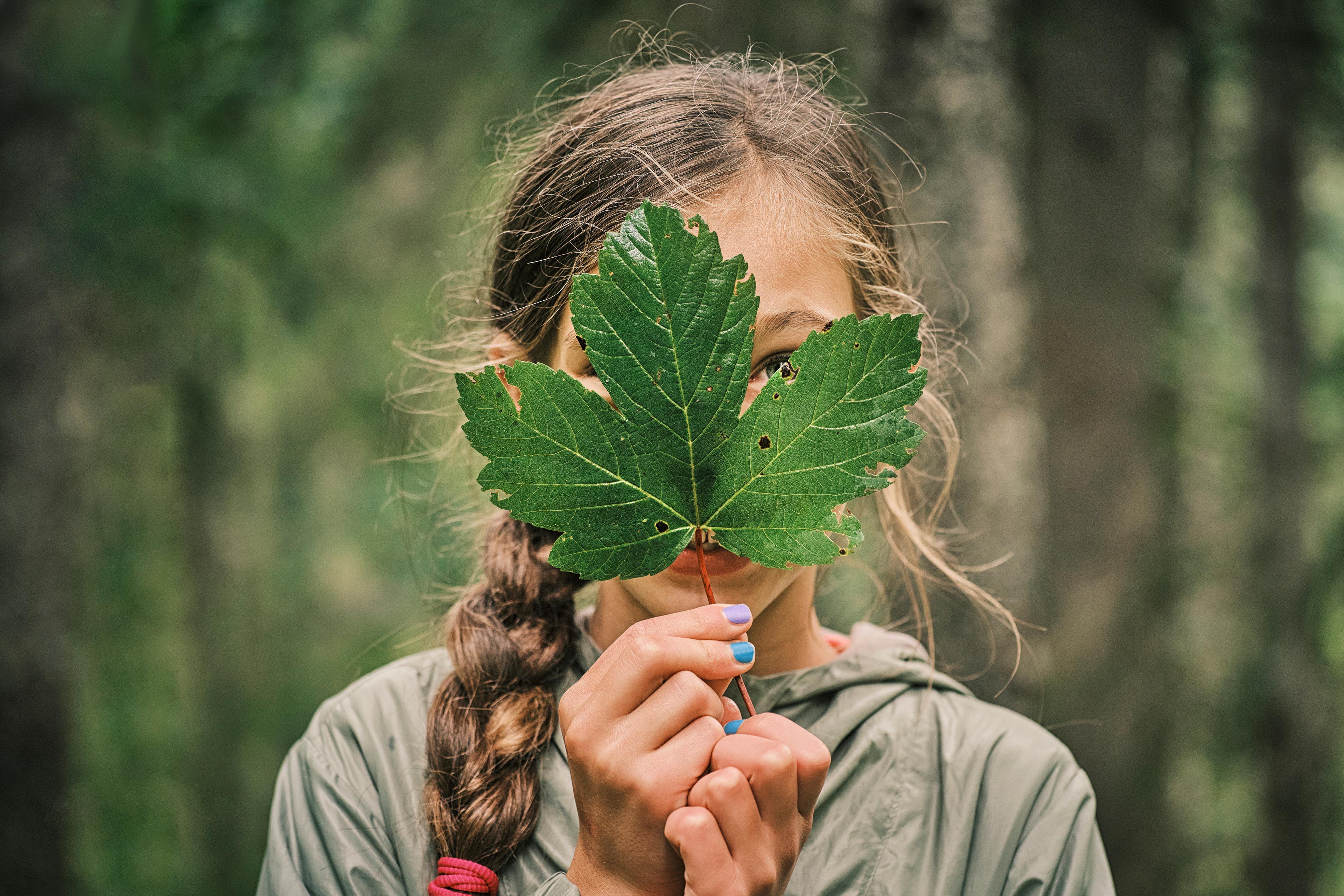 Girl covering face with green maple leaf