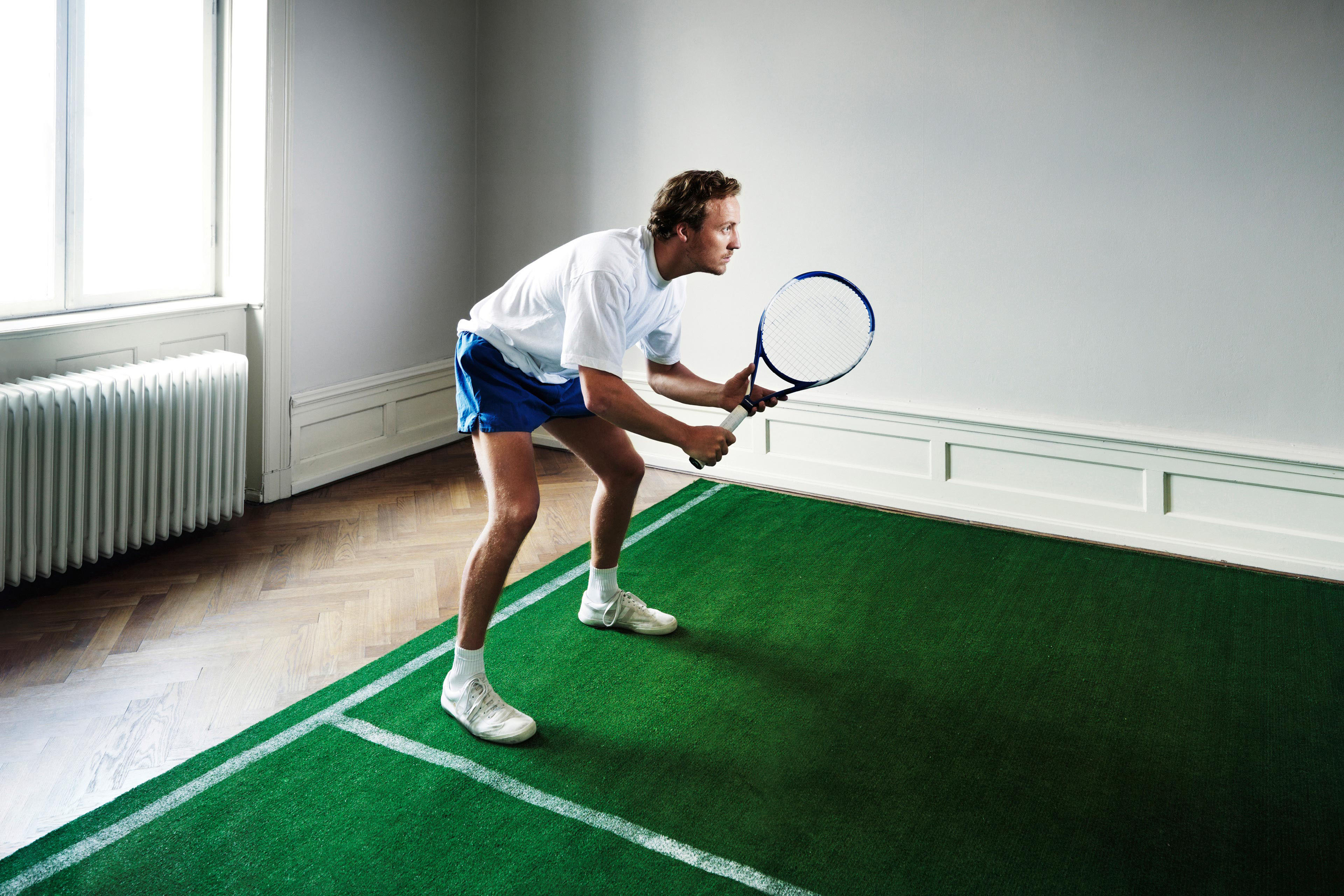 Männlicher Tennisspieler auf dem Hallenplatz im Zimmer