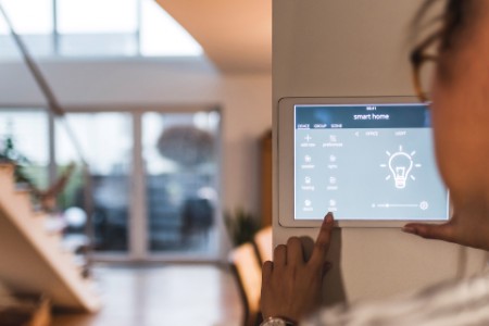 Frau benutzt Bildschirm mit Smart Home Control-Funktionen zu Hause