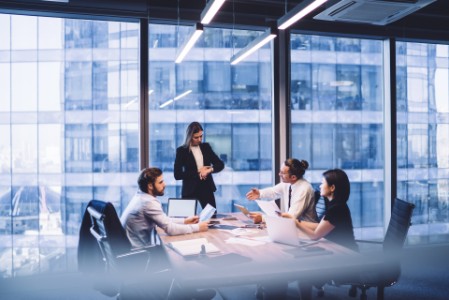 Diverse colleagues teamworking on project ideas sitting at desk with modern technology, successful female director checking time while intelligent multiracial partners brainstorming for cooperation