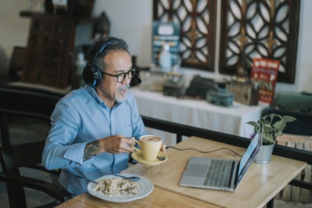 Mann vor Laptop in Telefonkonferenz mit Kaffee und Pasta neben sich
