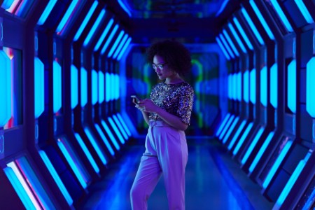 Junge Geschäftsfrau schaut in einem raumschiffartigen Korridor auf ihr Smartphone