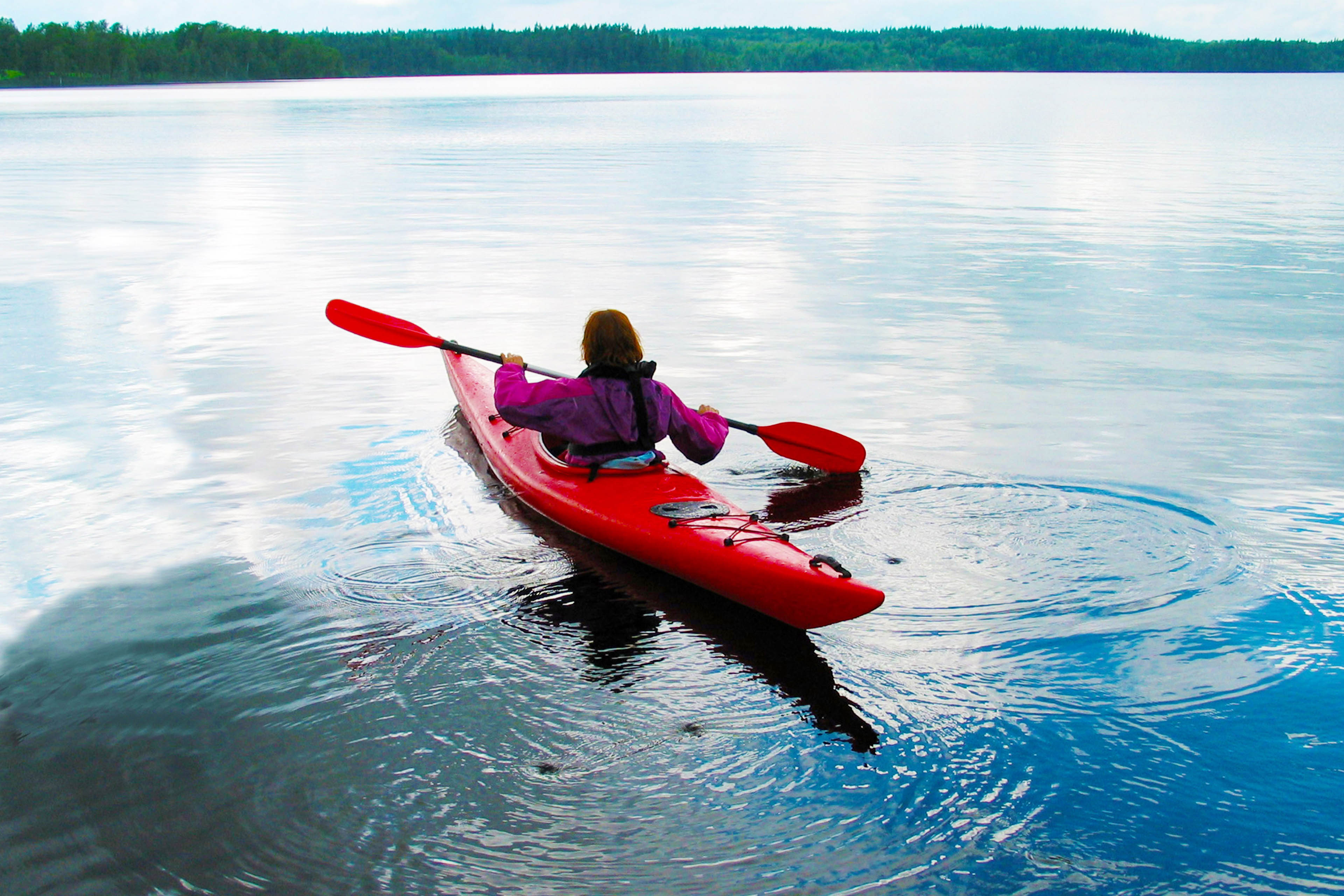 Woman kayaking on a big lake in Sweden background