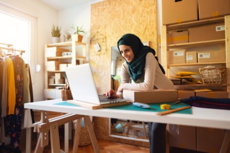 Smiling Muslim businesswoman with hijab using laptop 