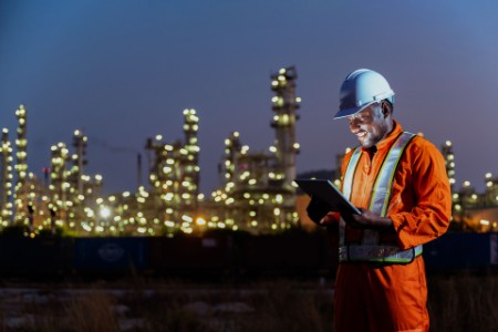 African engineer working on tablet inspecting oil refinery at night