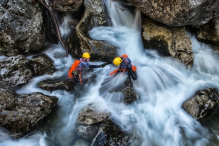 Two members of canyoning team helping each other to cross dangerous waterfall