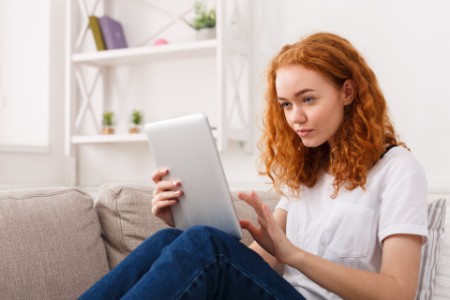 woman using a digital tablet sitting on couch at home