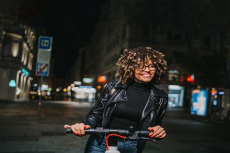 Beautiful young woman on electric scooter in the city at night