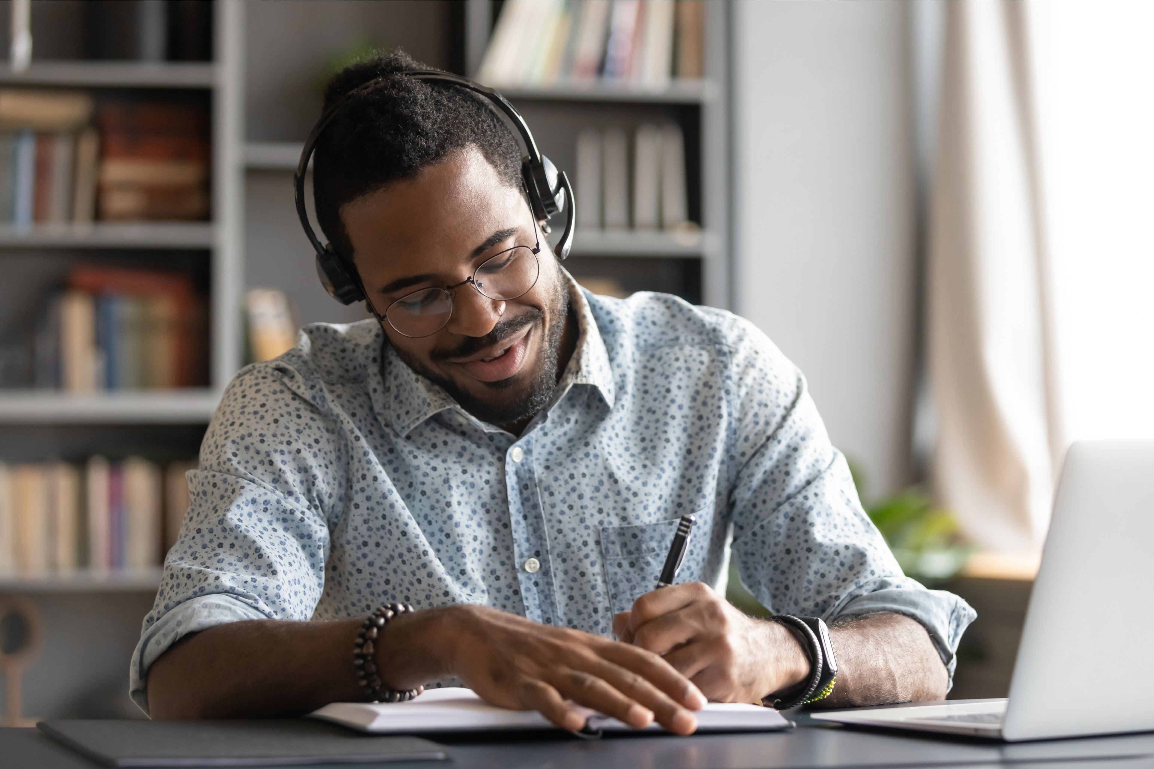 EY - Man wearing headphones taking notes while using laptop