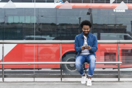 EY - Smiling stylish mid adult man using mobile phone while sitting at bus stop