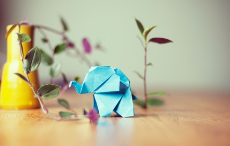 EY - A blue origami elephant on a table with a plant next to it.