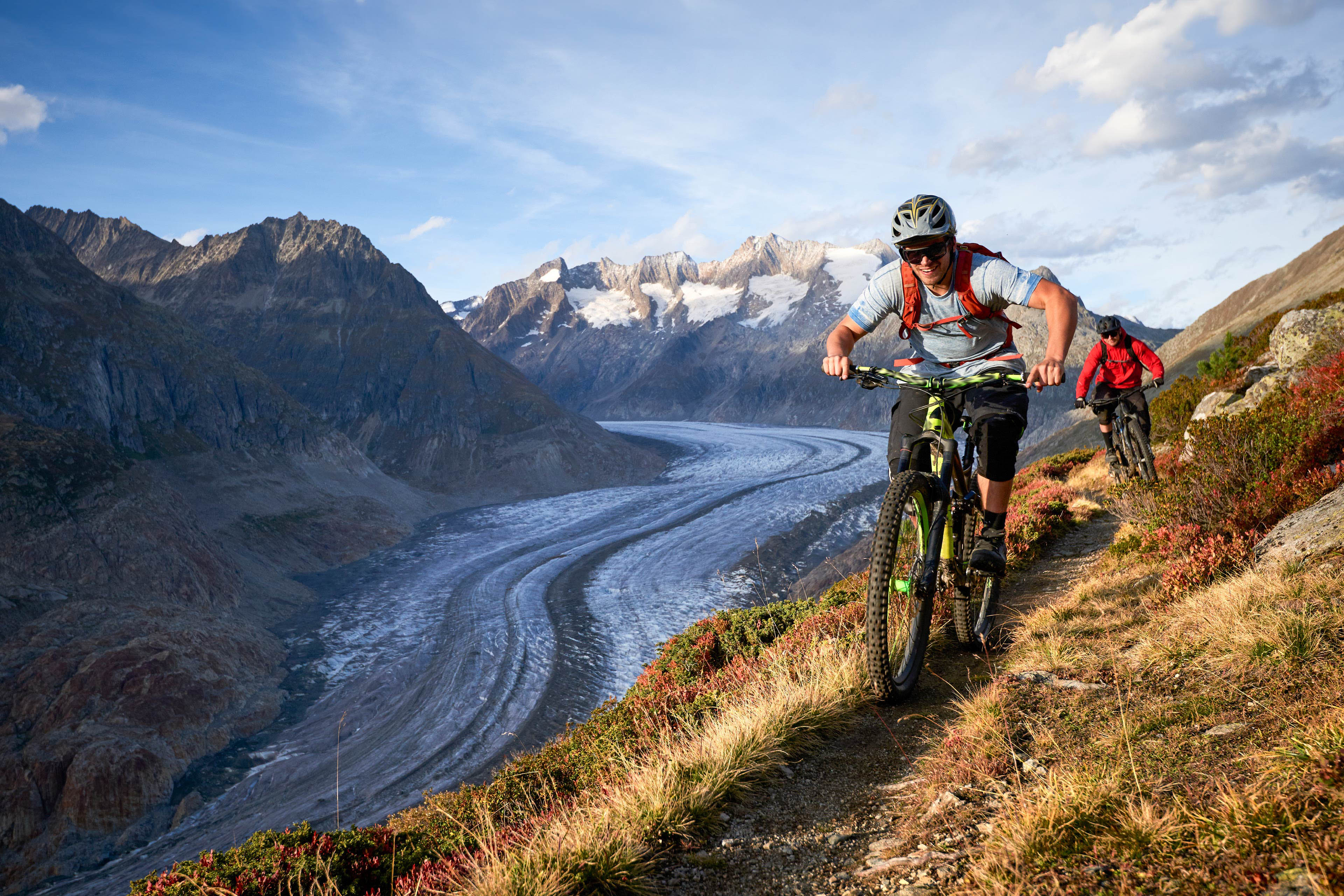 Mountain bikers ride narrow trail above glacier