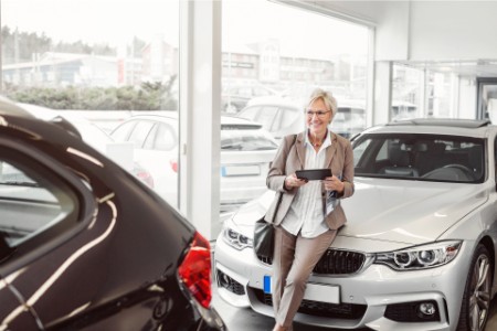 Businesswoman with digital tablet looking at car in showroom