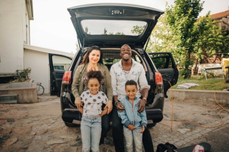 Portrait of smiling family leaning on car trunk in front yard
