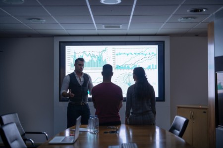 Команда на фоне интерактивного экрана с графиками проводит деловую встречу