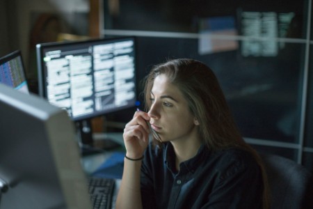 Mujer sentada en un escritorio rodeada de monitores que muestran datos