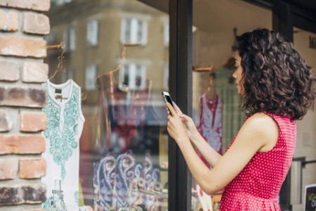 Mixed race woman taking cell phone photograph of clothes in store window