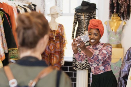 Young woman with camera phone photographing friends shopping in clothing store