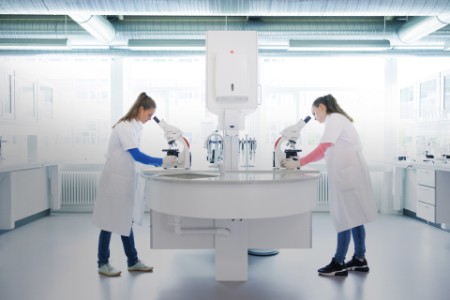 Dos científicas de pie en un laboratorio mirando a través de microscopios