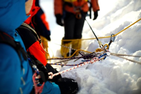 Alpinistas a subir montanha com neve e a verificar o equipamento