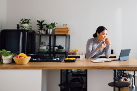Asian businesswoman using digital tablet at kitchen desk.
