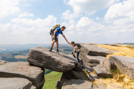 Male hiker helping female friend for climbing mountain during vacations on sunny day