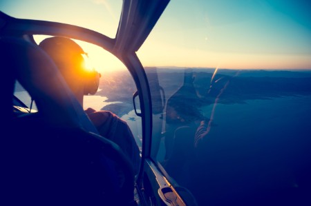Vista de la cabina de mando de un pequeño avión y piloto sobre el agua con el sol bajo en el horizonte