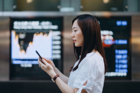 Mujer de negocios usando un teléfono inteligente contra la pantalla que muestra el mercado de valores