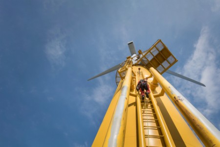 Engineer climbing ladder of wind turbine from boat at offshore windfarm