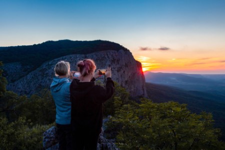 female couple taking pictures of sunset in mountains at dusk