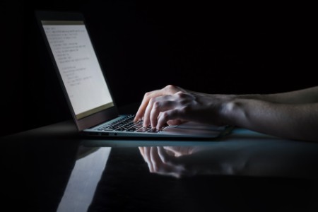 hands typing text on laptop at night
