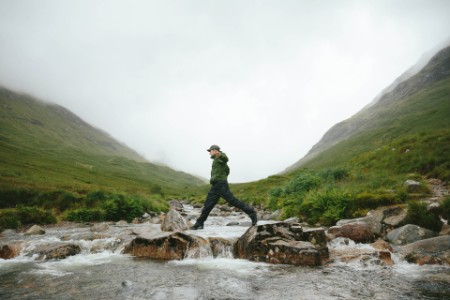 Caminante que cruza el río en Mountain Valley, Glencoe, Escocia