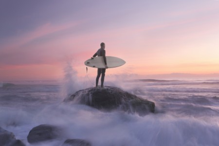 Surfer on rock against sunset, water around