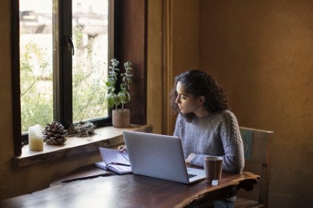 Mujer trabaja desde casa usando un ordenador portátil y un libro de referencia